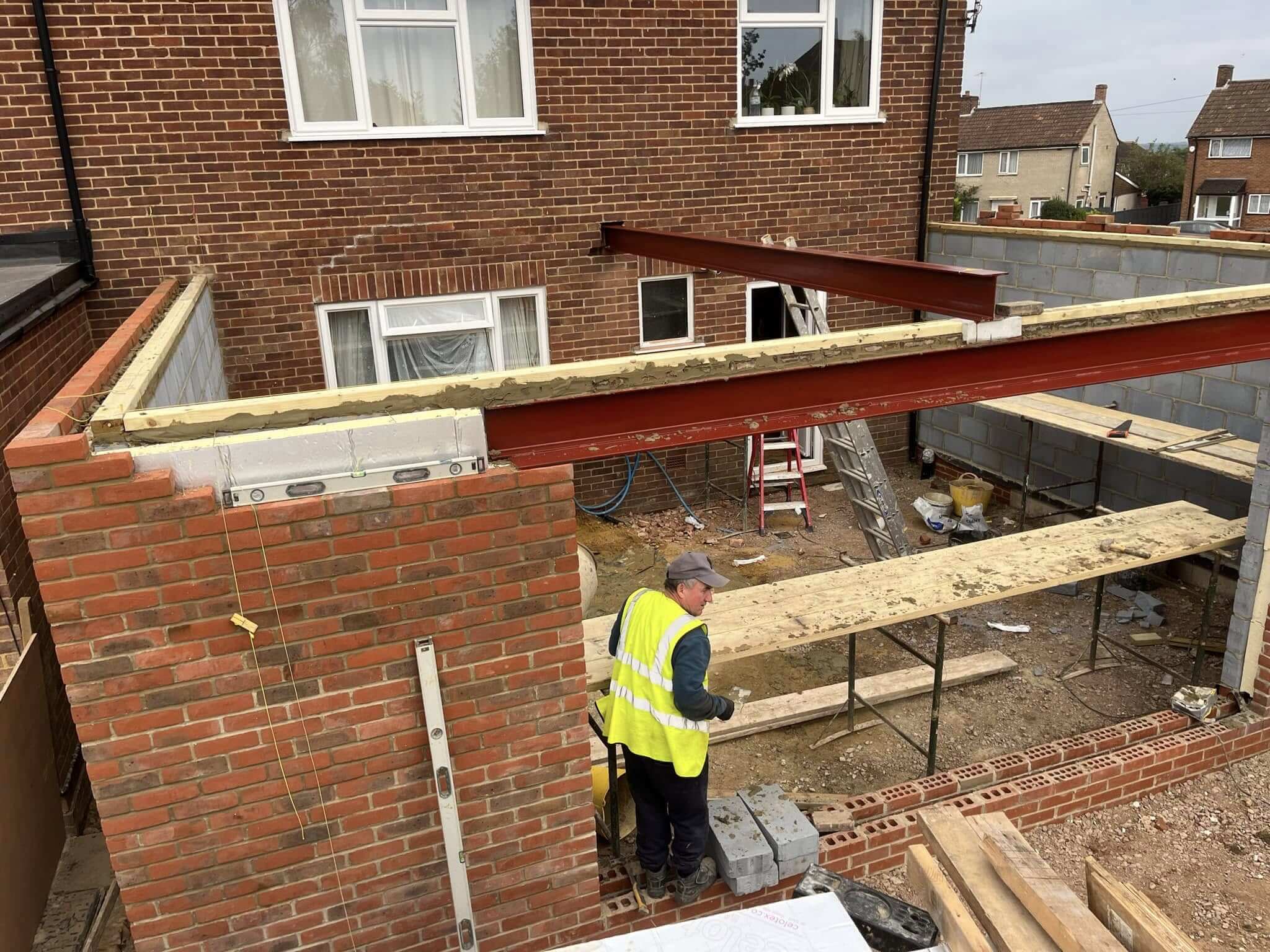 Builder in hi-vis installing a structural steel beam between two brick walls