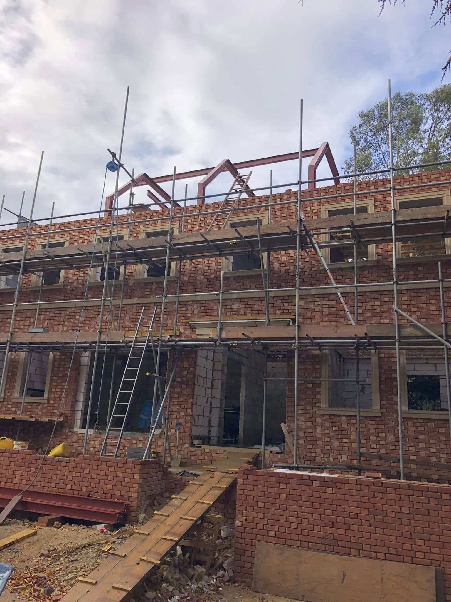 New build home with red brickwork and timber roof structure under scaffolding